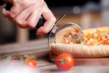 Image showing Slicing fresh pizza with roller knife. 