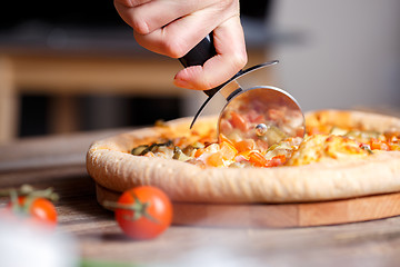 Image showing Slicing fresh pizza with roller knife. 