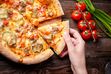 Image showing Hand picking tasty slice of pizza lying on wooden table