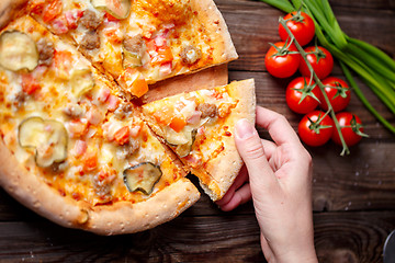 Image showing Hand picking tasty slice of pizza lying on wooden table