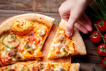 Image showing Hand picking tasty slice of pizza lying on wooden table