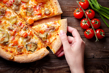 Image showing Hand picking tasty slice of pizza lying on wooden table