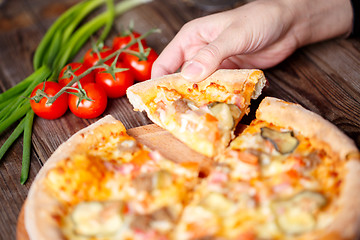 Image showing Hand picking tasty slice of pizza lying on wooden table