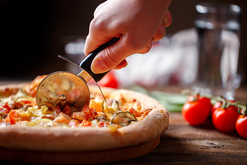 Image showing Slicing fresh pizza with roller knife. 