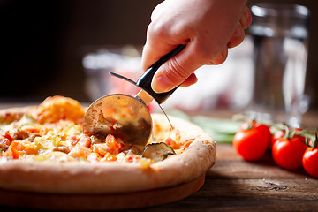 Image showing Slicing fresh pizza with roller knife. 