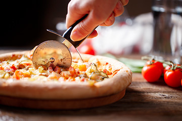 Image showing Slicing fresh pizza with roller knife. 