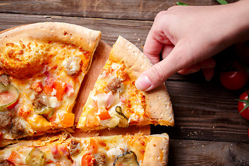 Image showing Hand picking tasty slice of pizza lying on wooden table