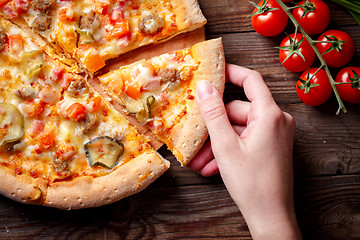 Image showing Hand picking tasty slice of pizza lying on wooden table