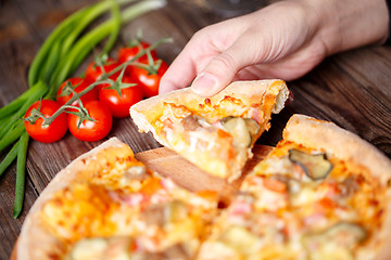 Image showing Hand picking tasty slice of pizza lying on wooden table