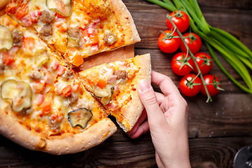 Image showing Hand picking tasty slice of pizza lying on wooden table