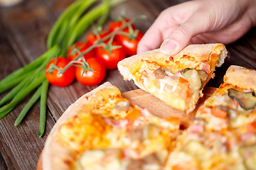 Image showing Hand picking tasty slice of pizza lying on wooden table