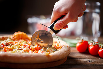 Image showing Slicing fresh pizza with roller knife. 