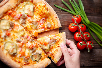 Image showing Hand picking tasty slice of pizza lying on wooden table