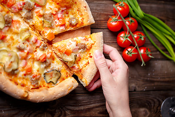 Image showing Hand picking tasty slice of pizza lying on wooden table