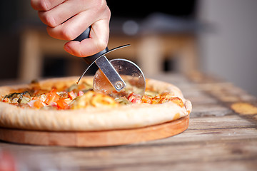 Image showing Slicing fresh pizza with roller knife. 