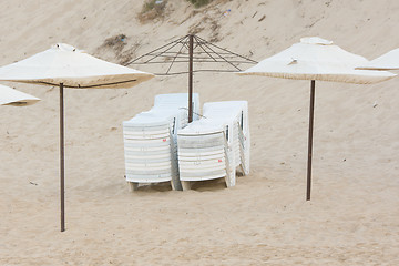 Image showing Two stacks of folded chairs on the beach with umbrellas