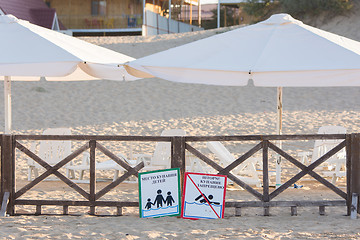 Image showing Anapa, Russia - September 21, 2015: Signs a - place children bathing, storm, swimming prohibited - lie on the sandy beach near the fence with a parasol