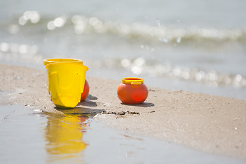 Image showing Childrens toy dishes items left on the sandy shore by the water
