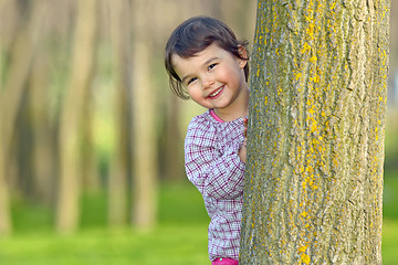 Image showing Little girl hiding behind a tree
