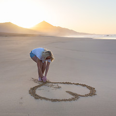 Image showing Lady drawing heart shape in sand on beach.