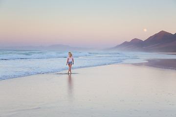 Image showing Lady walking on sandy beach in sunset.