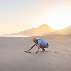 Image showing Lady drawing heart shape in sand on beach.