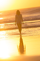 Image showing Lady walking on sandy beach in sunset.