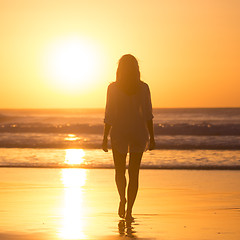 Image showing Lady walking on sandy beach in sunset.