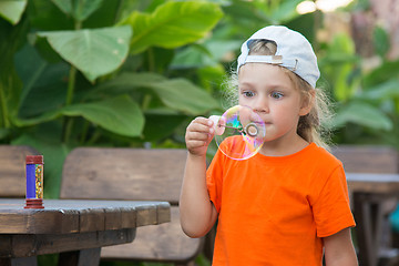 Image showing  Little girl in a bright T-shirt inflates large bubble in the street