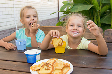 Image showing Satisfied children at a table in the courtyard eating pancakes with sour cream