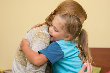Image showing The four-year daughter hugging her mother sitting on the bed in the room