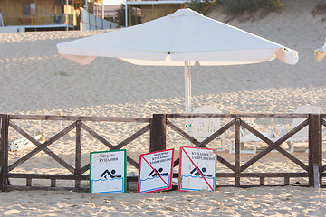 Image showing Anapa, Russia - September 21, 2015: Signs a - place children bathing, storm, swimming prohibited - lie on the sandy beach near the fence with a parasol