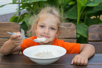 Image showing Little girl smiling at a wooden table on a background of green eating porridge