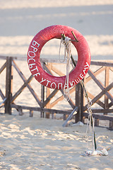 Image showing Lifebuoy throw a drowning man with a sign hanging on a rusty metal stick on the sandy beach