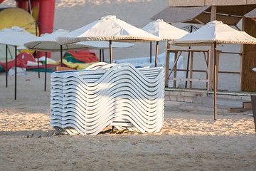 Image showing Stacked chairs in the evening on the beach under the umbrellas