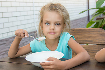 Image showing Six year old girl at a wooden table in the yard eating porridge