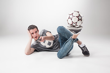 Image showing The portrait of fan with ball, holding  tv remote on white background