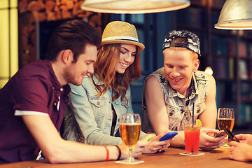 Image showing happy friends with smartphones and drinks at bar