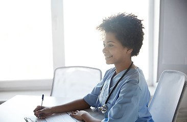 Image showing happy female doctor or nurse writing at hospital