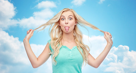 Image showing happy young woman showing tongue and holding hair