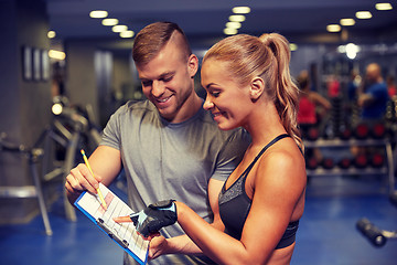 Image showing smiling woman with trainer and clipboard in gym