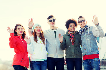 Image showing happy teenage friends waving hands on city street