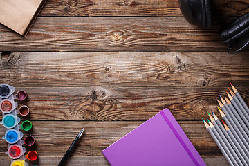 Image showing Watercolors, color pencils and sketchbook on wooden table. Flat lay photo with empty space for logo, text.