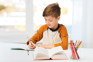 Image showing smiling student boy writing to notebook at home