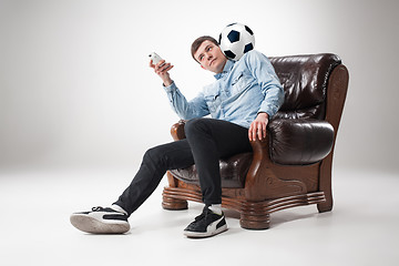 Image showing The portrait of fan with ball, holding  tv remote on white background