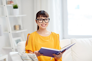 Image showing smiling young asian woman reading book at home