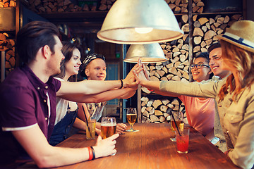 Image showing happy friends with drinks making high five at bar