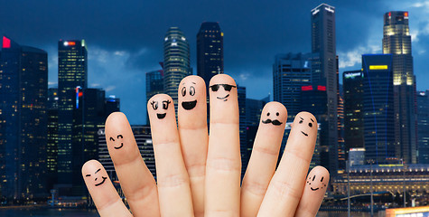 Image showing close up of fingers with smiley faces over city