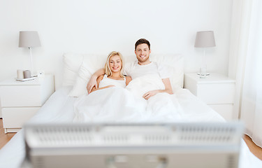 Image showing happy couple lying in bed at home and watching tv