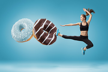 Image showing Fit young woman fighting off bad food on a blue background